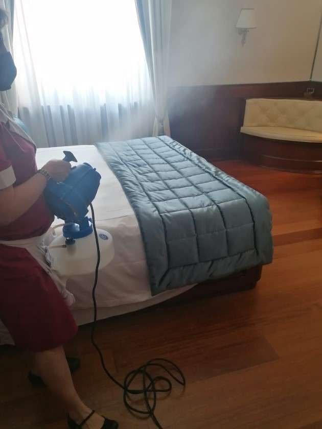 Una persona utilizza un nebulizzatore portatile per disinfettare un letto rifatto in una camera d'albergo.