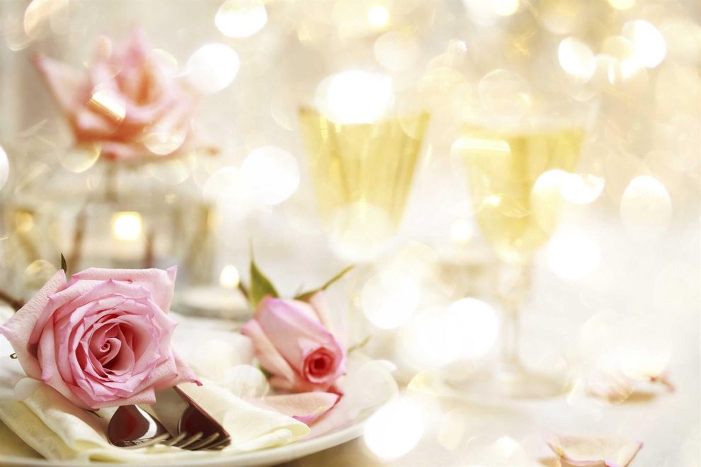 Un plato blanco coronado con rosas rosadas y cubiertos sobre una mesa.
