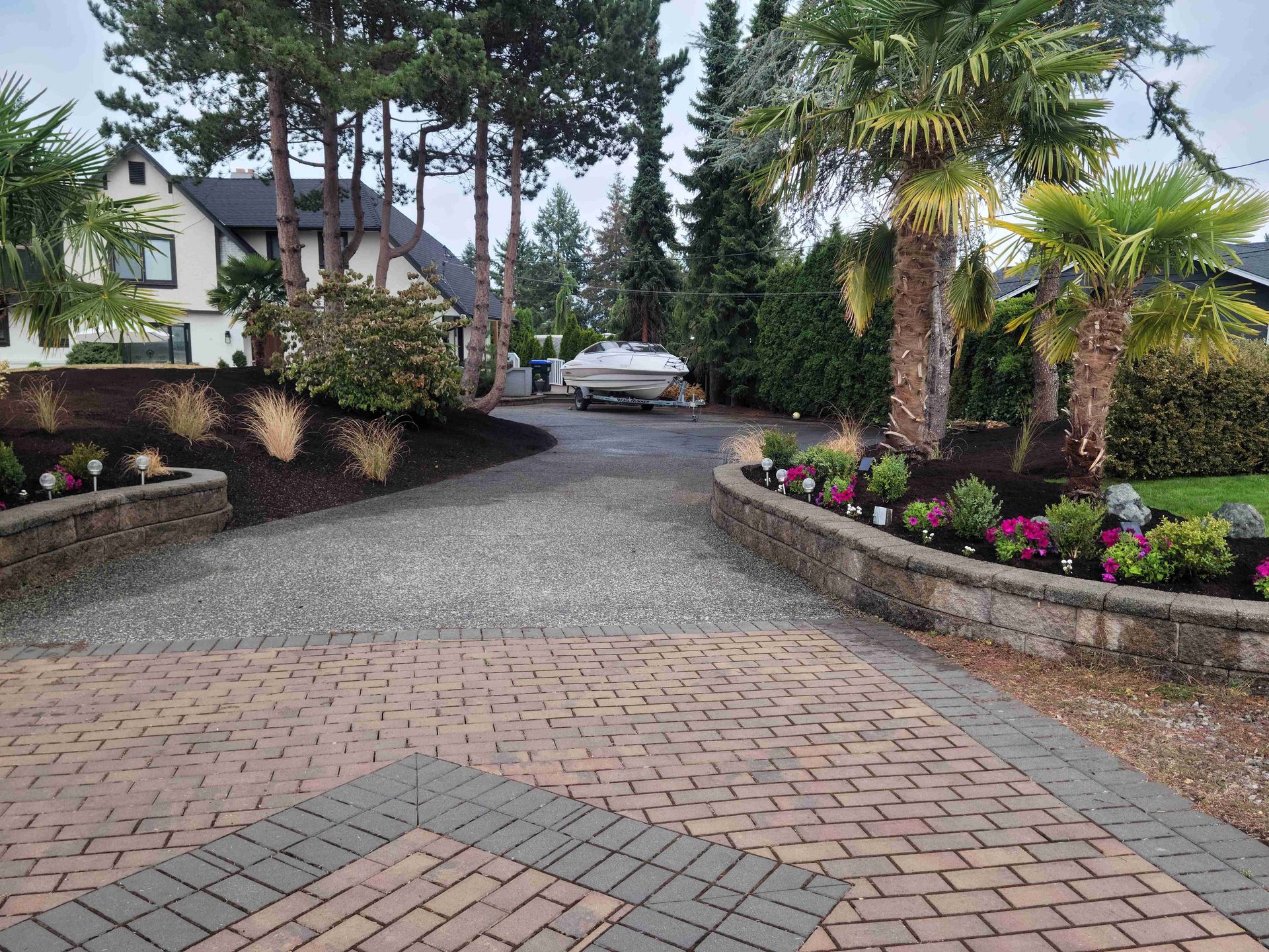 A brick driveway leading to a house with a boat in the background.