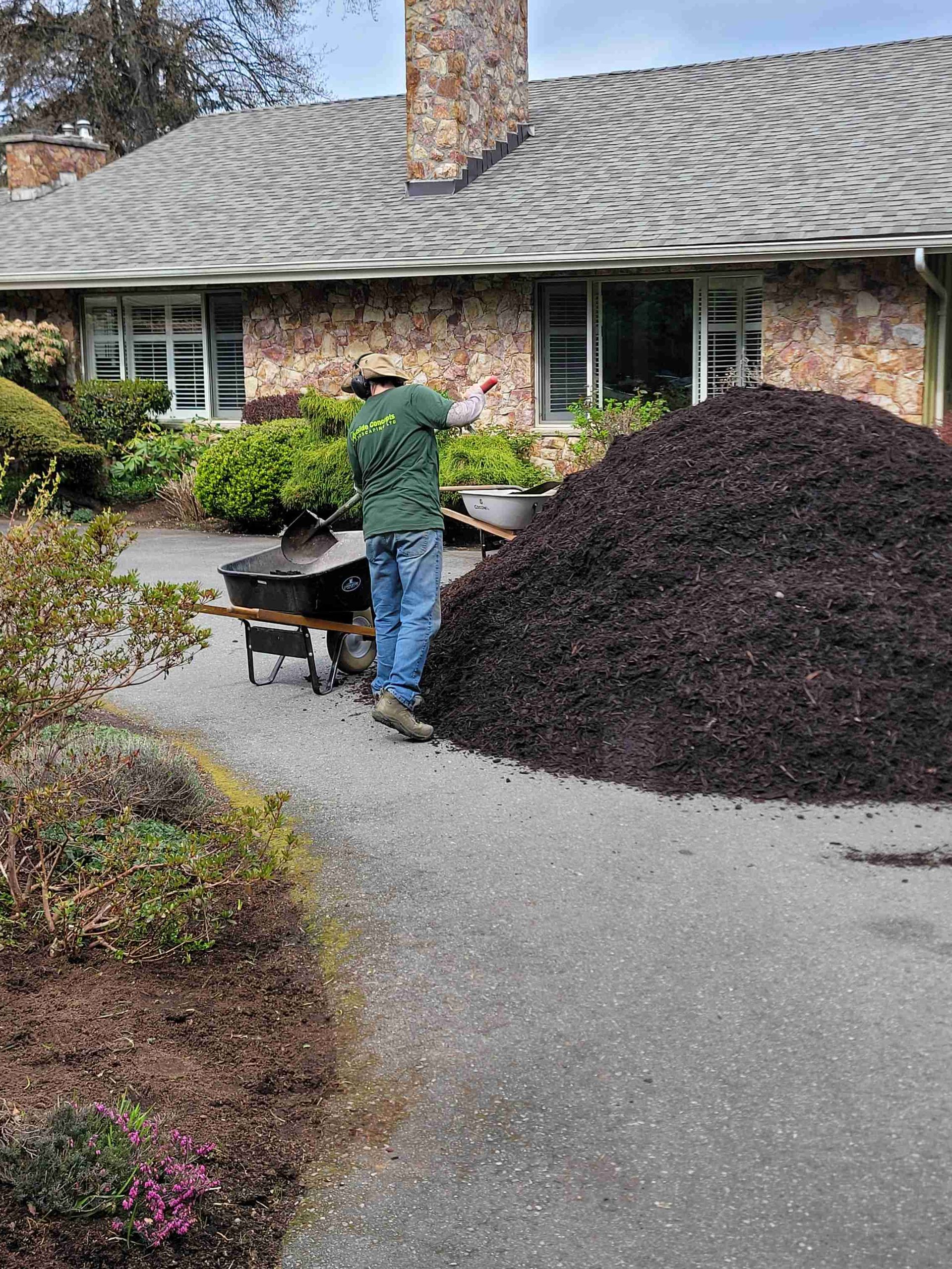 A man is standing next to a pile of mulch in front of a house.