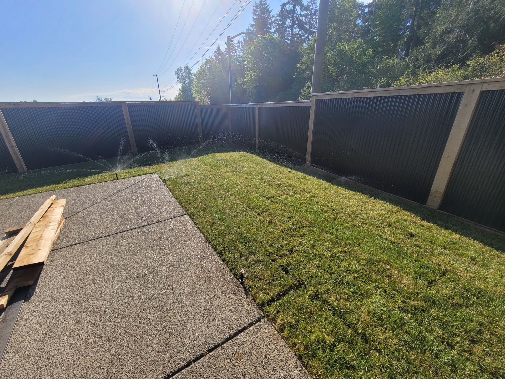 Backyard with grass, concrete patio, and wooden fence in bright sunlight