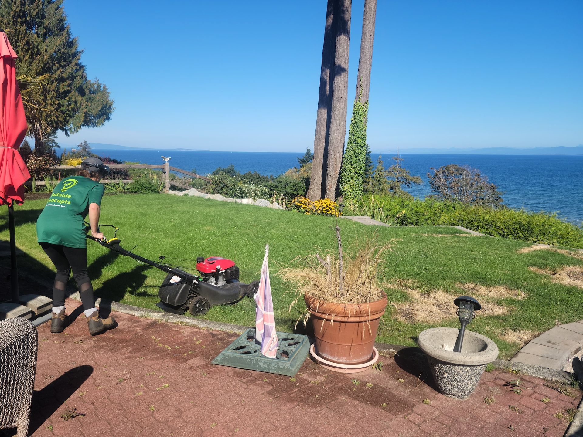 A woman is mowing a lawn with a view of the ocean