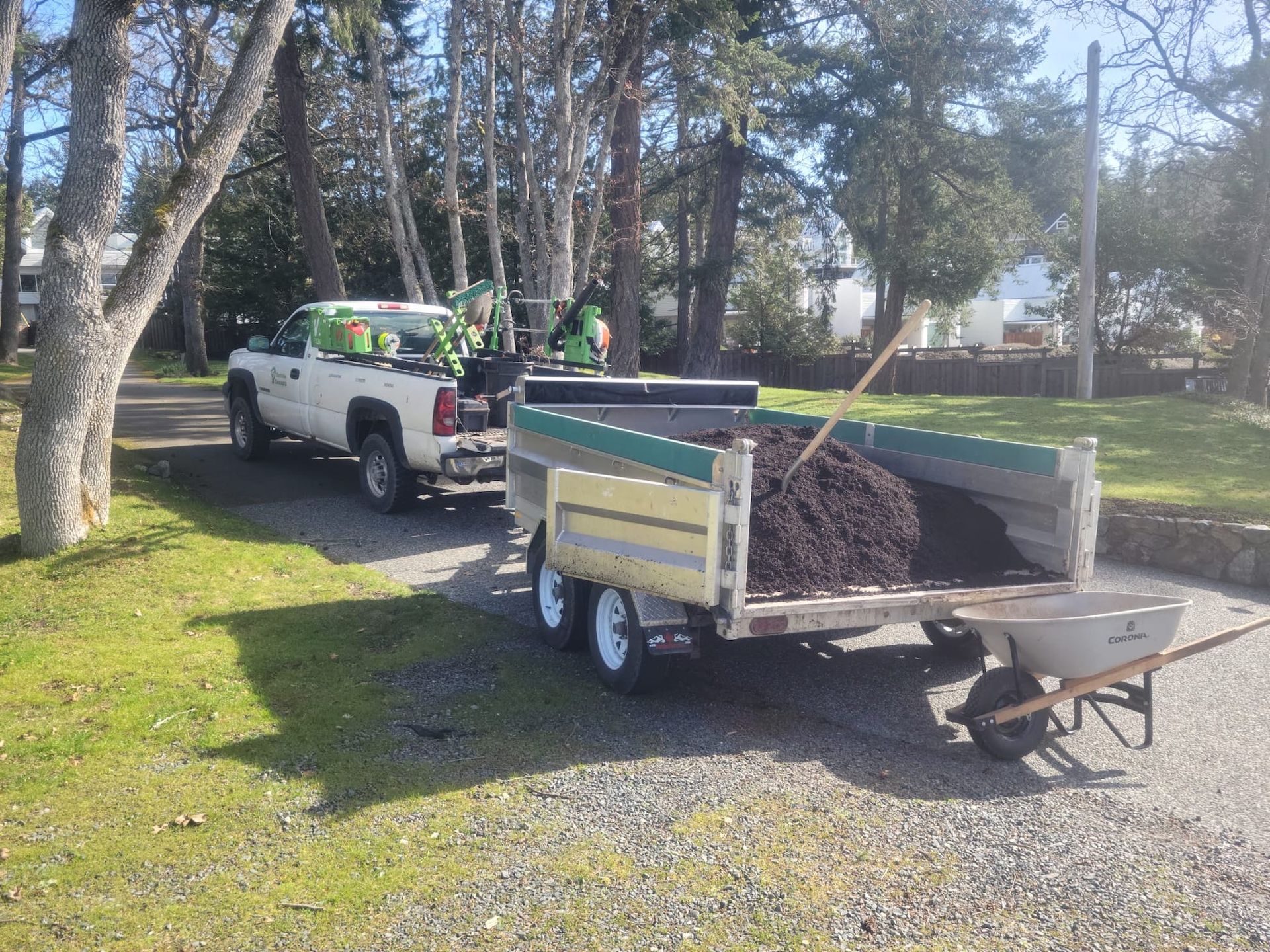 A white truck is pulling a trailer full of dirt.