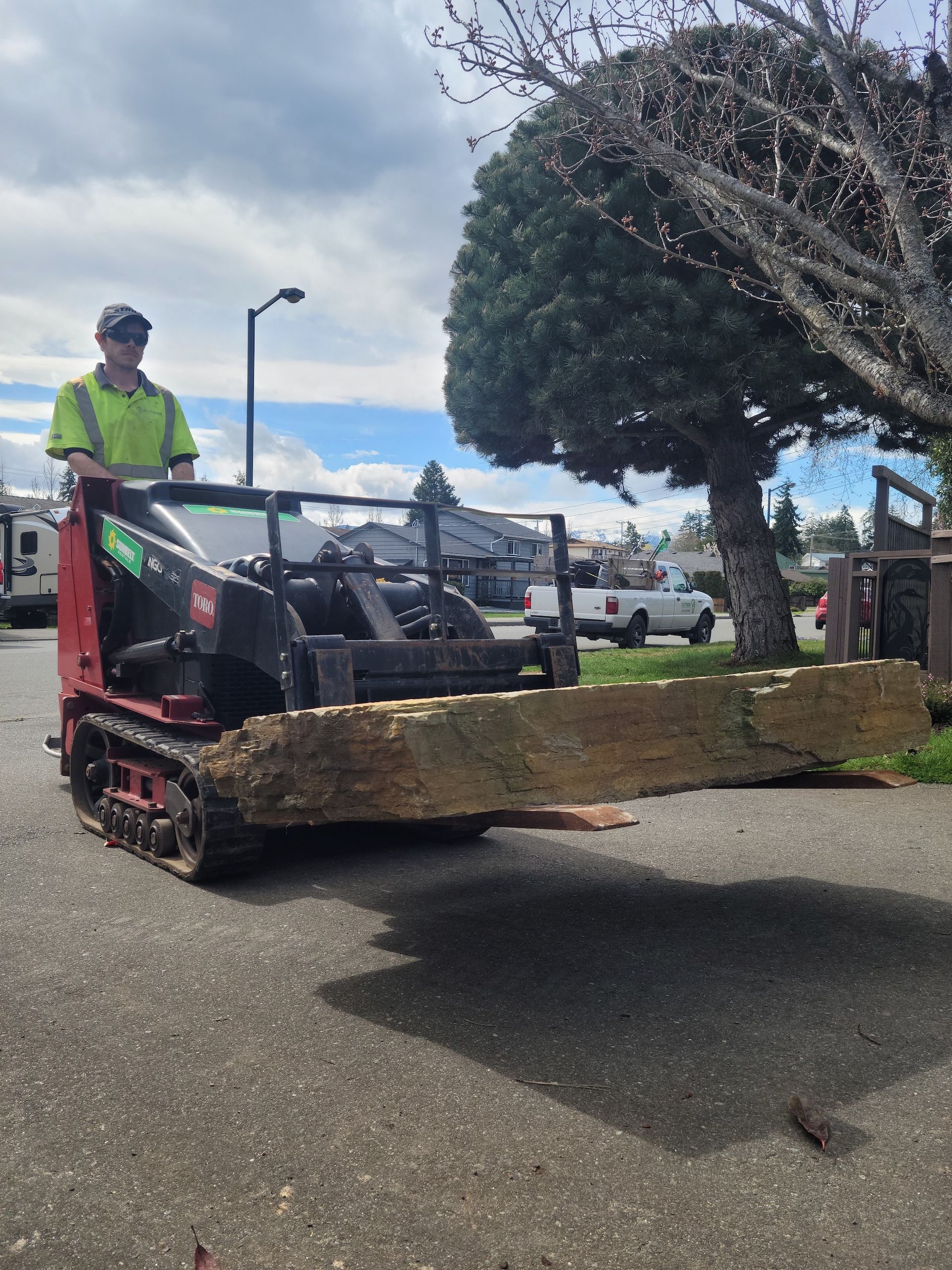 A man is driving a tractor with a large piece of wood on it.