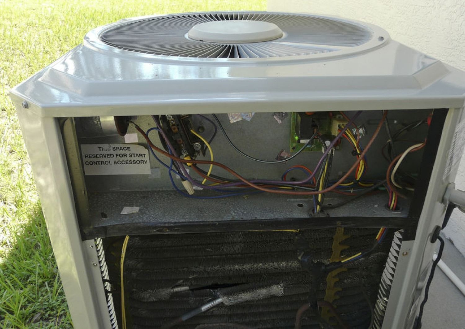 Open air conditioning unit, gray box with wiring and fan, outdoor setting, close-up view.