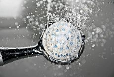 Water spraying from a silver shower head with a blue-colored interior, creating droplets against a blurred background.