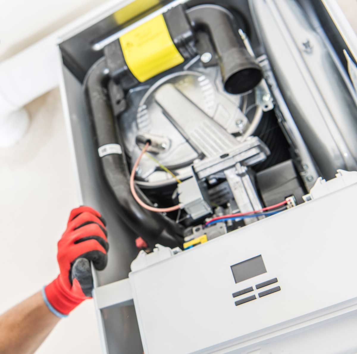 Person with red gloves working on a white furnace with open access panel.