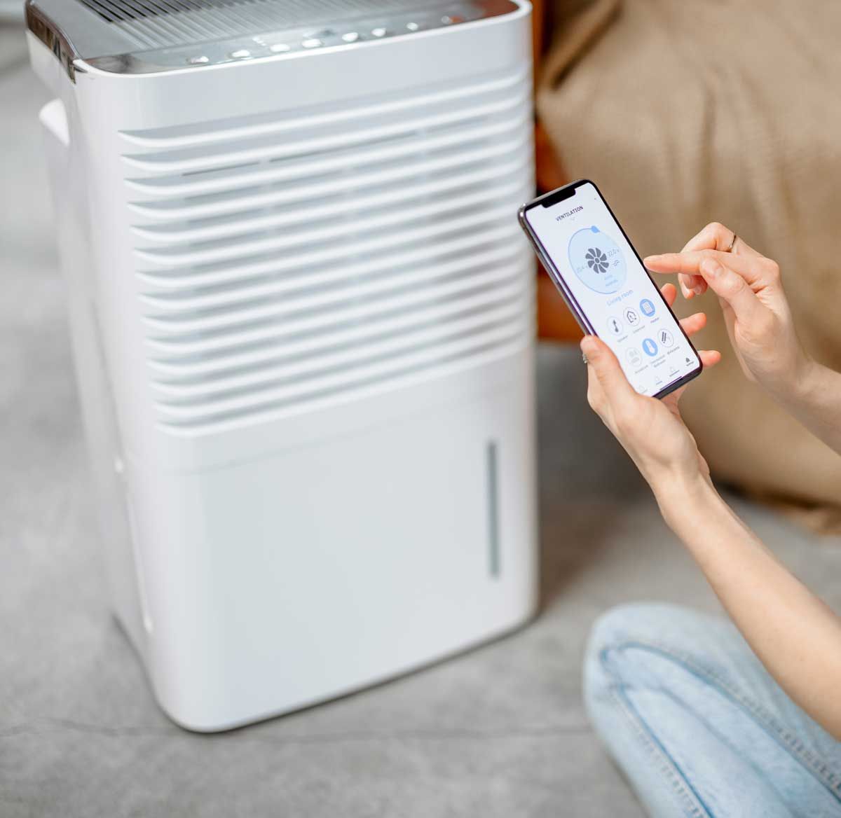 Woman using phone to control a white dehumidifier in a room.
