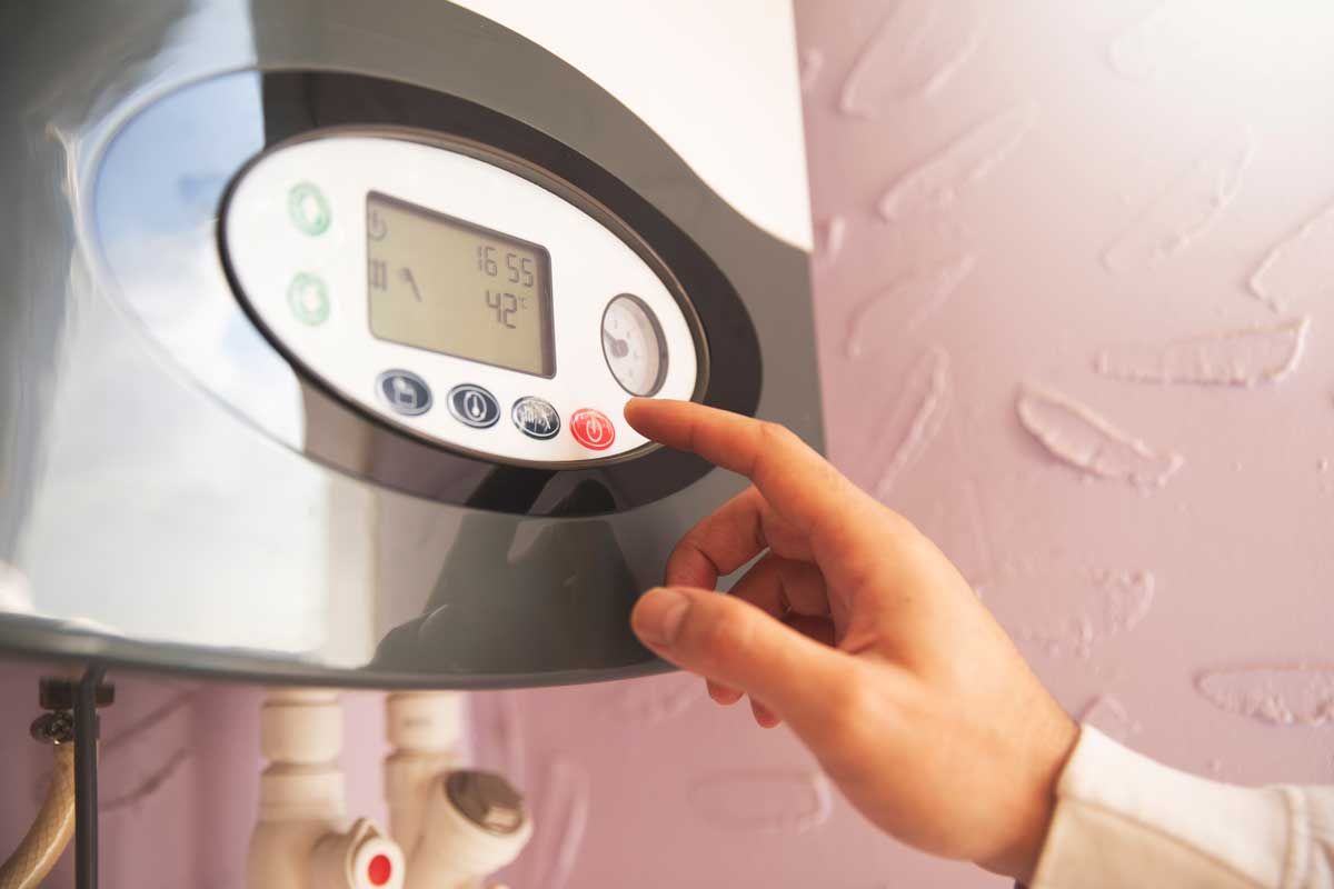 Hand adjusting the control panel on a water heater, set against a pink wall.