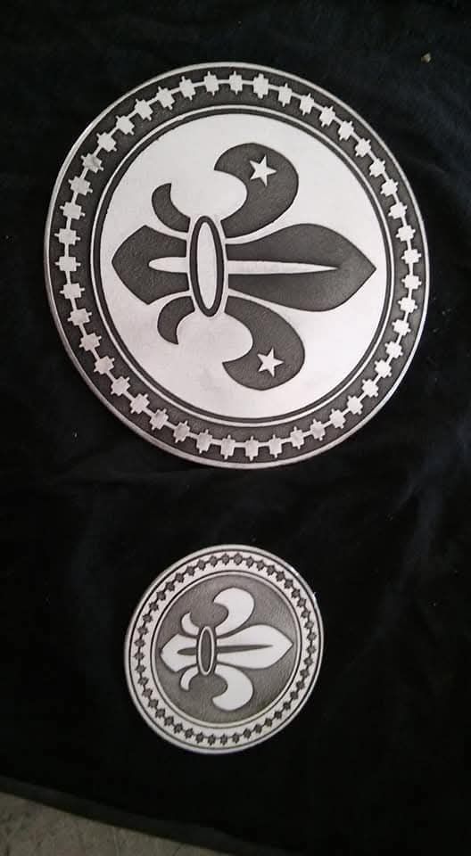 Dos emblemas circulares en blanco y negro con una mariposa estilizada y estrellas sobre un fondo de tela oscura.