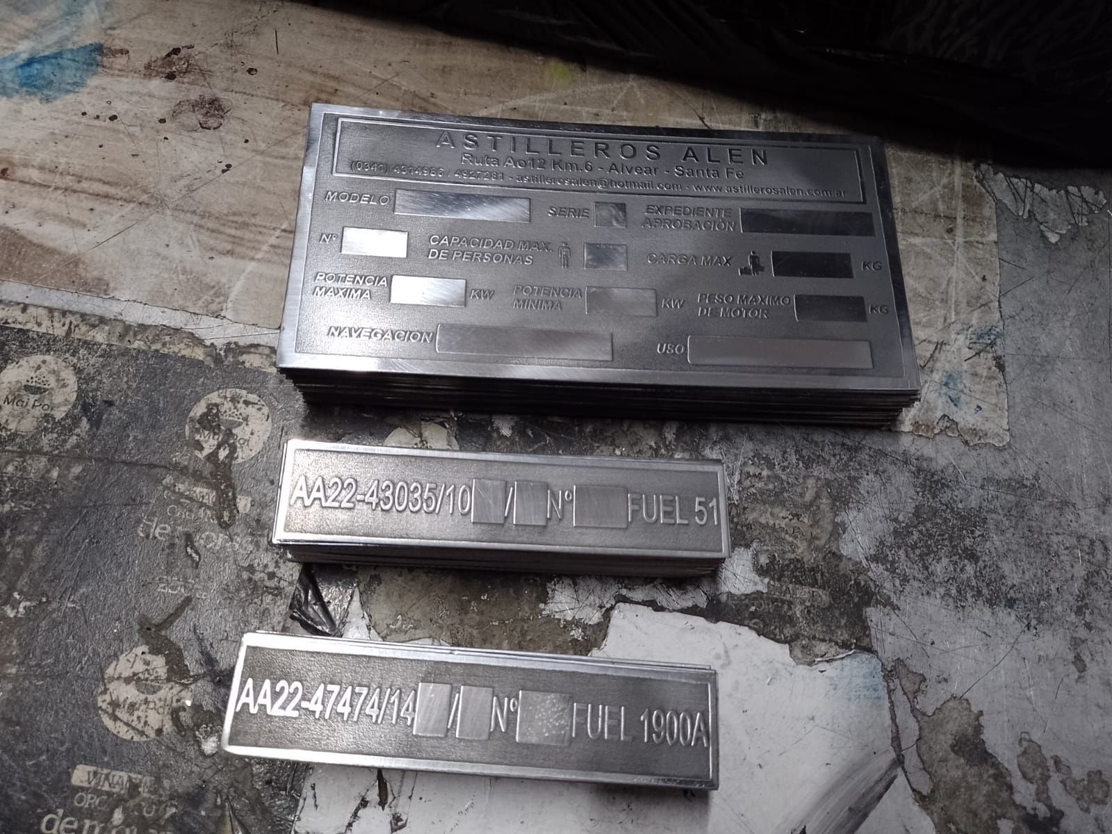 Tres placas de identificación metálicas y una caja sobre un suelo de hormigón rugoso.