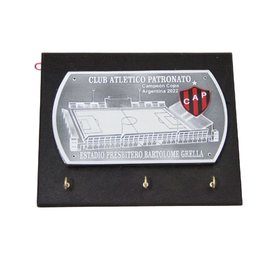 Placa de pared negra con una placa plateada del club Atlético Patronato y tres ganchos dorados debajo.