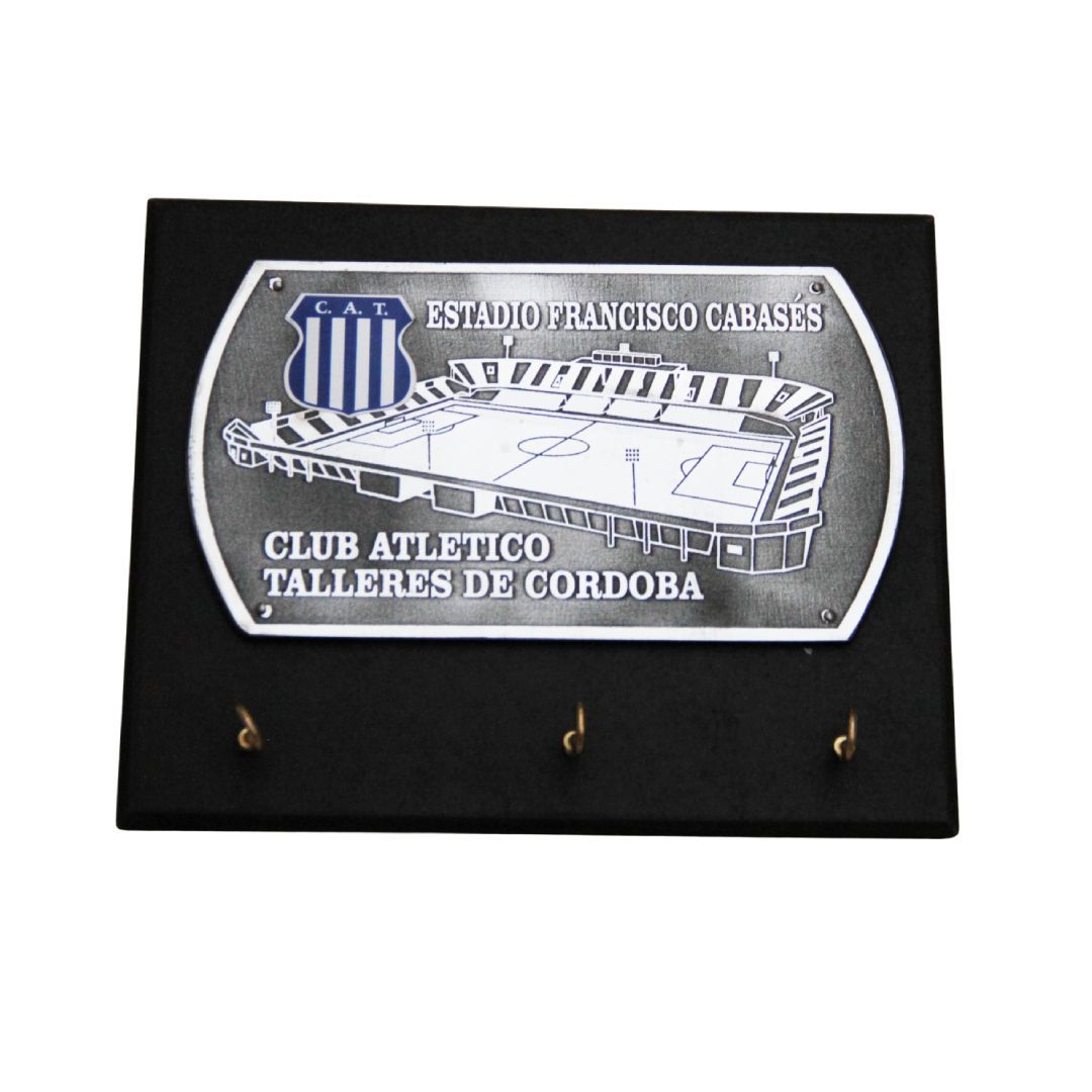 Placa negra con un grabado plateado de un estadio con la inscripción “Club Atlético Belgrano” y tres ganchos debajo.