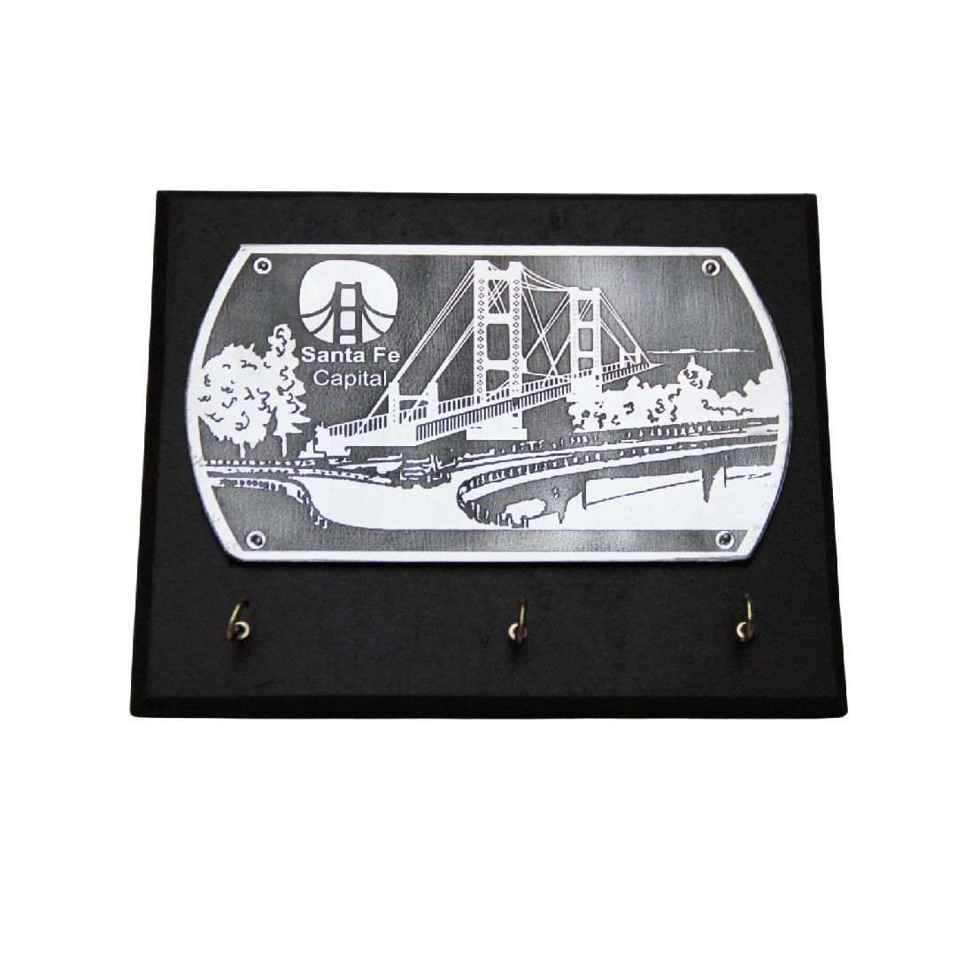 Placa de pared negra con una escena de puente grabada en blanco y tres ganchos debajo.