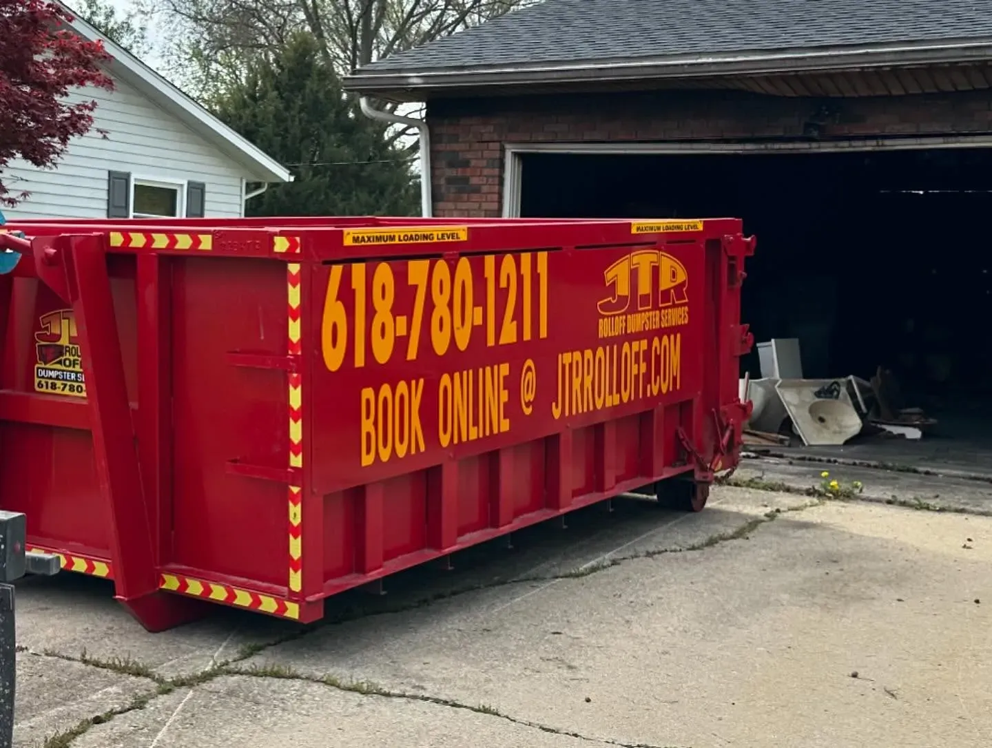 A red dumpster is parked in front of a garage.