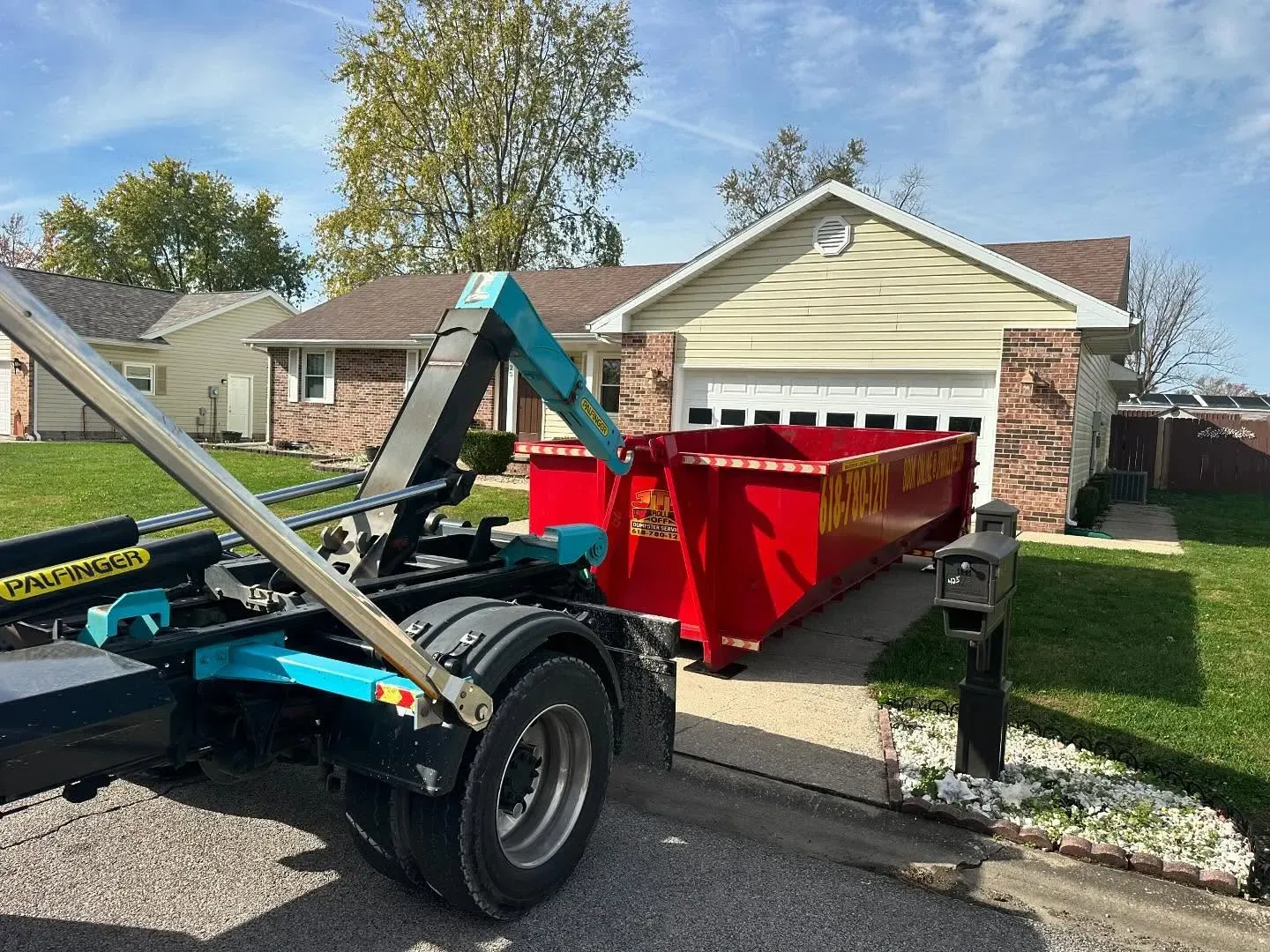 A dumpster is being loaded into a truck in front of a house.