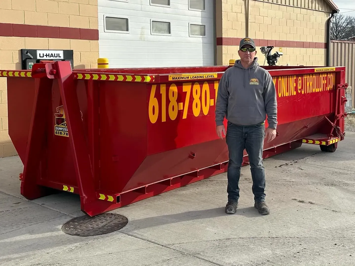 A man is standing in front of a large red dumpster.