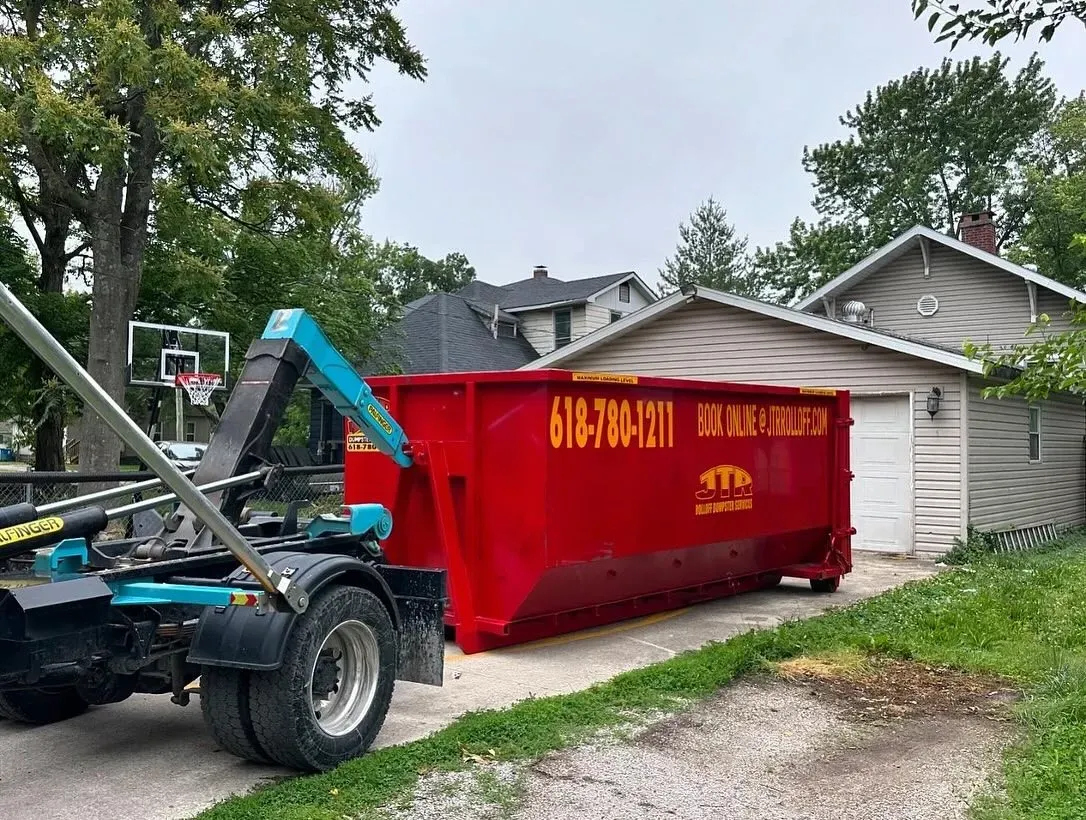 A red dumpster is sitting in a driveway next to a house.