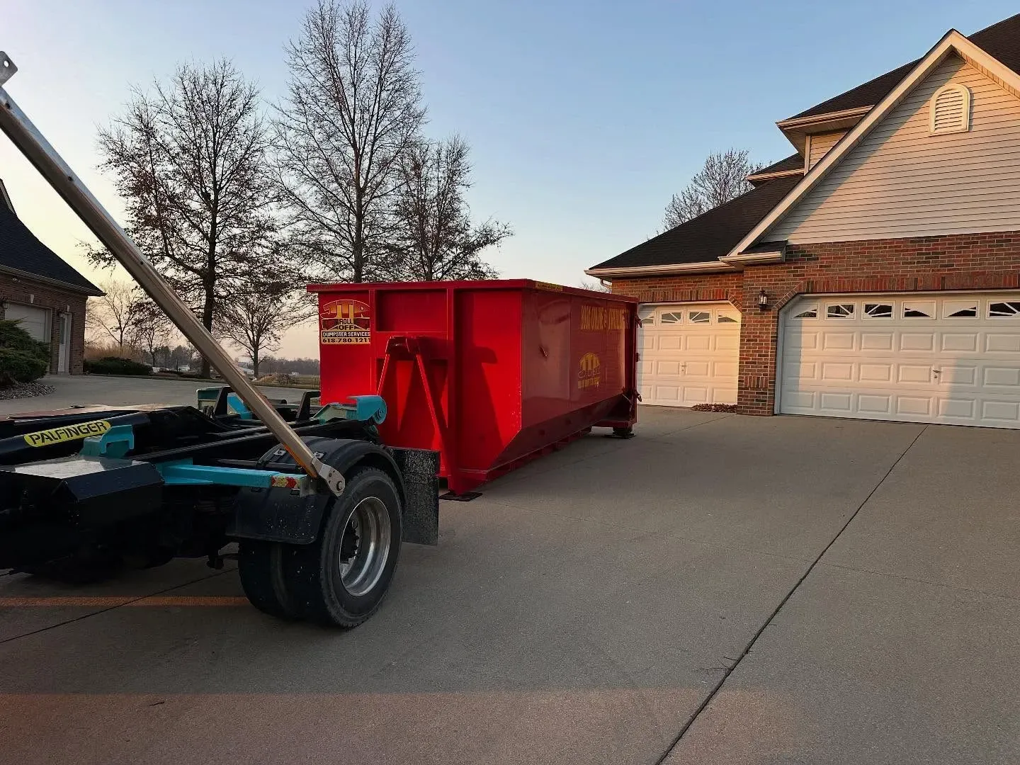 A red dumpster is being towed by a truck in a driveway.