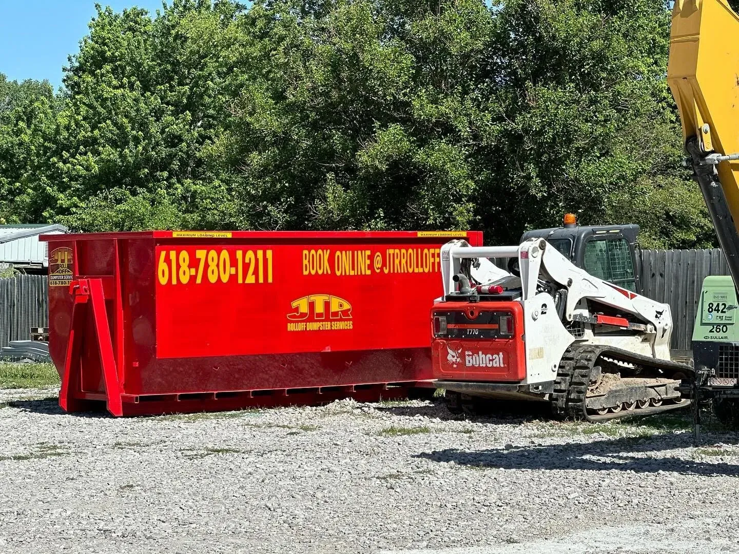 A red dumpster is parked next to a bulldozer.