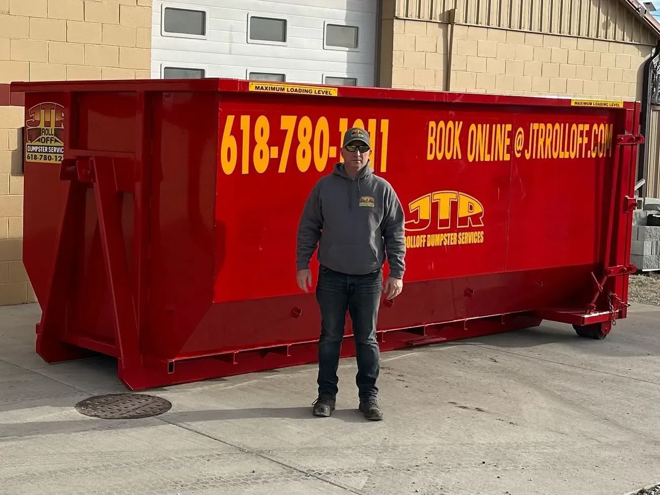A man is standing in front of a large red dumpster.