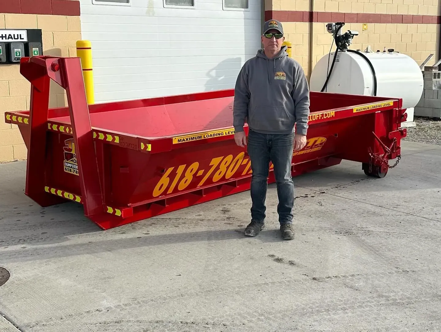 A man standing next to a red dumpster that says 618-780