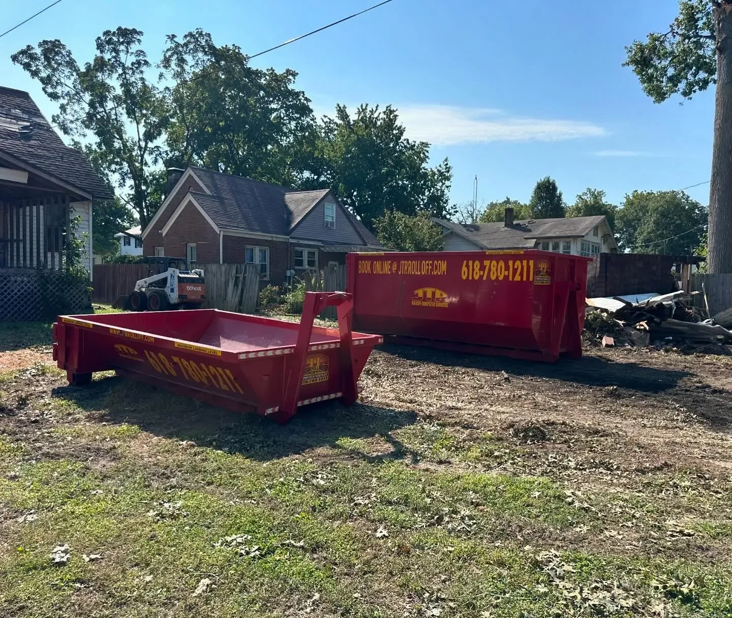 A red dumpster is sitting in a grassy field next to a house.