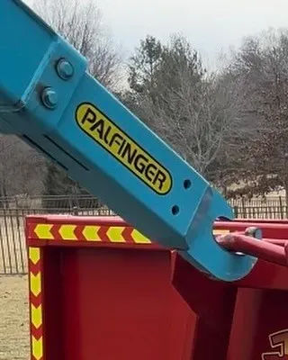 A blue palfinger crane is attached to a red dumpster.