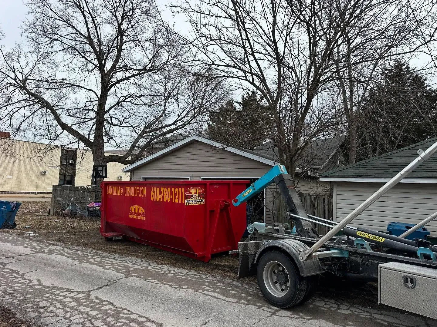 A red dumpster is sitting on the side of a road next to a house.