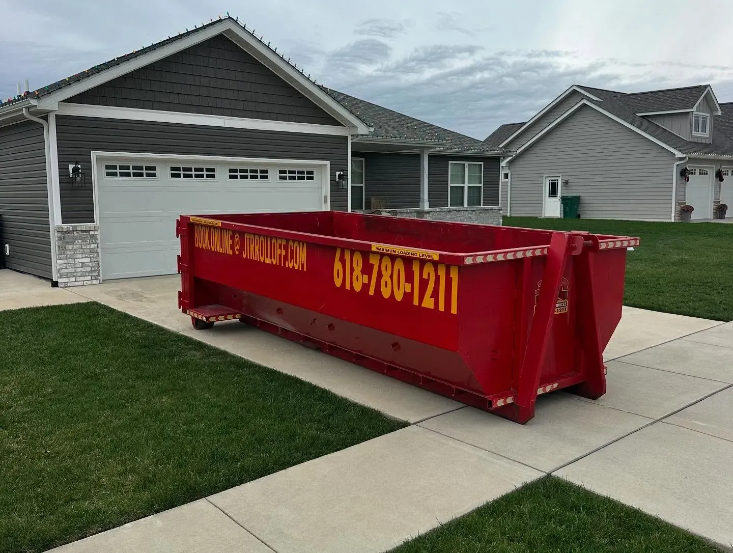 A large red dumpster is parked in front of a house.