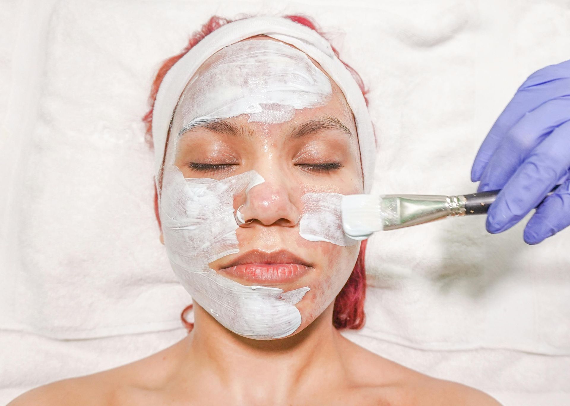 Facial mask being applied with a brush to a person lying with eyes closed