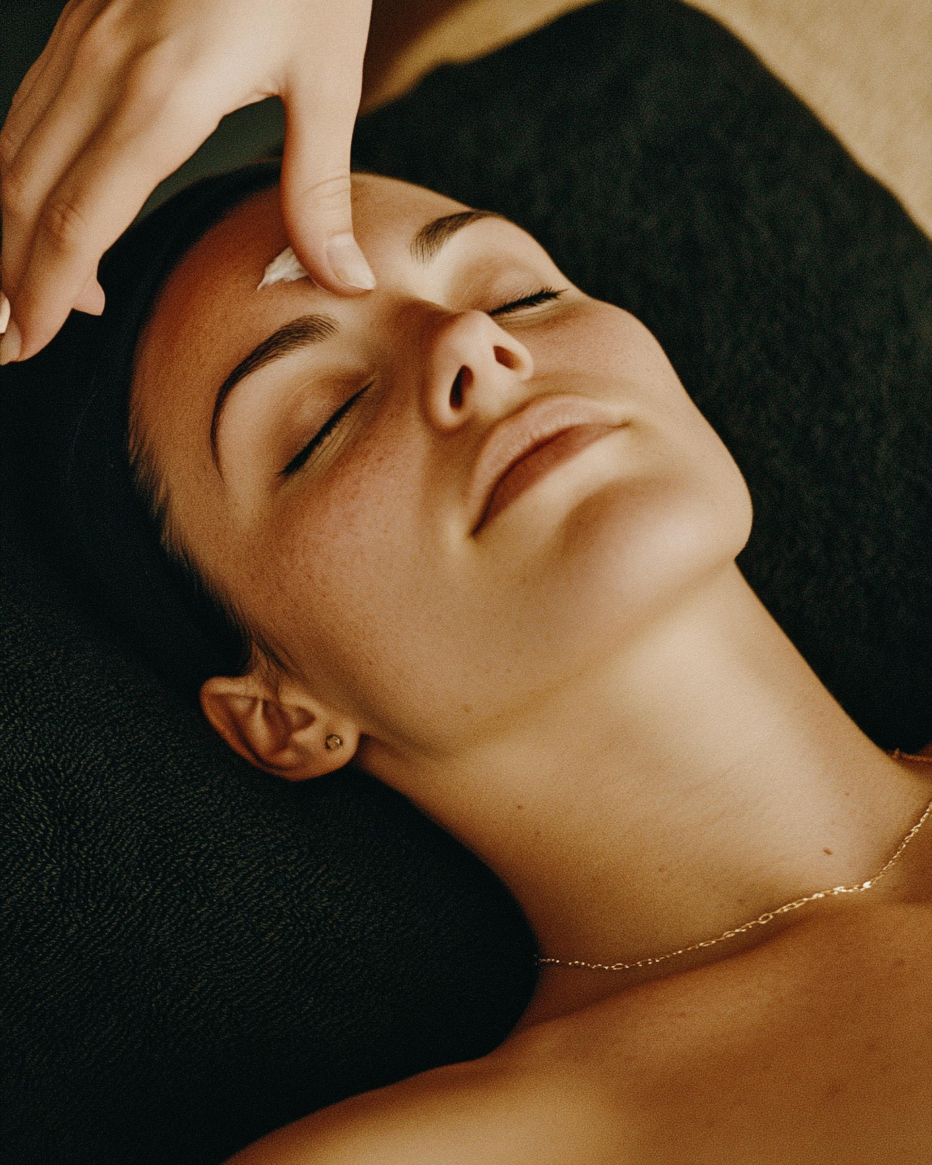 Person relaxing with eyes closed while a hand gently presses the forehead on a dark towel