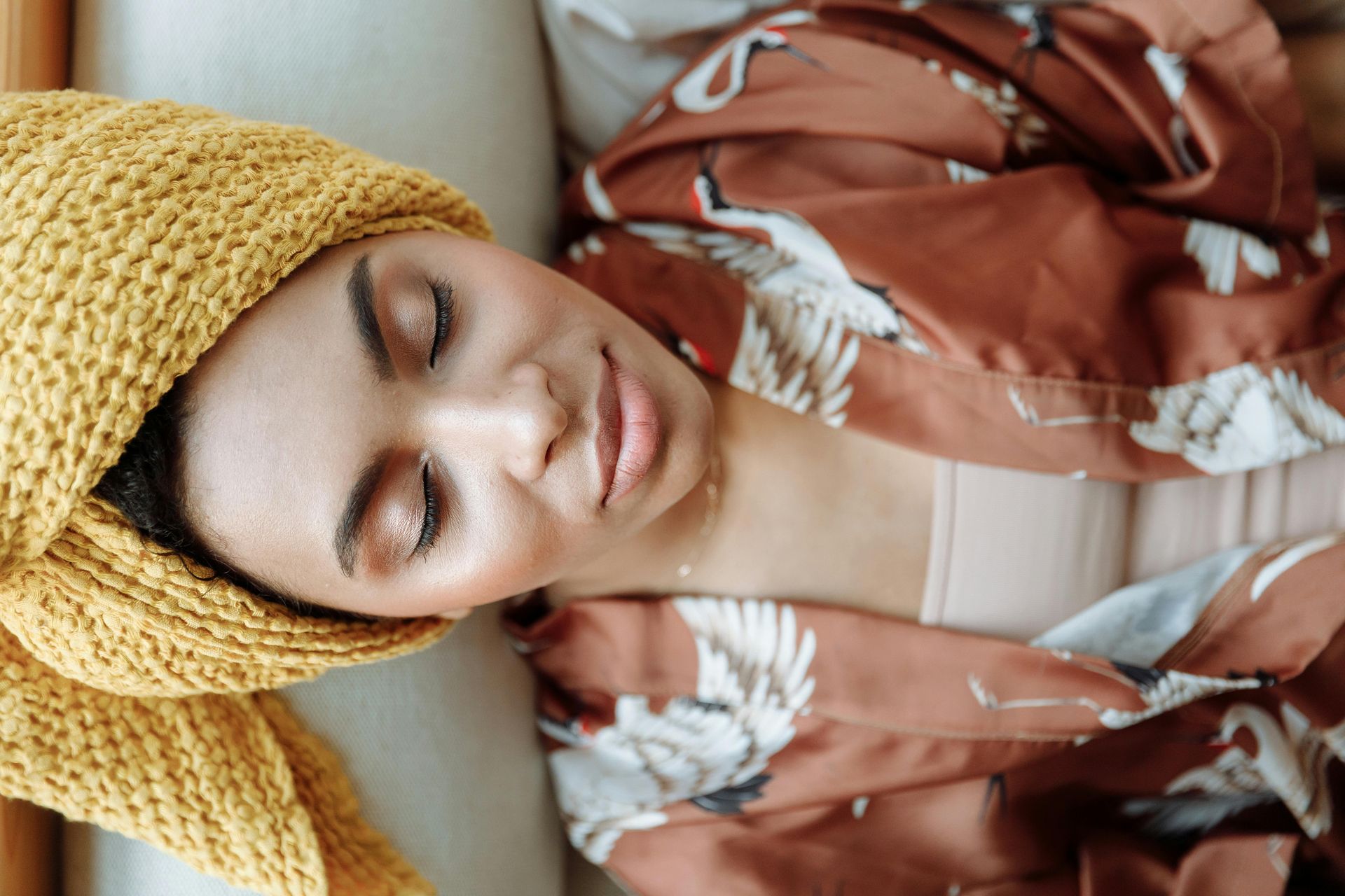 Woman sleeping on a couch, wrapped in a floral robe and mustard knit blanket