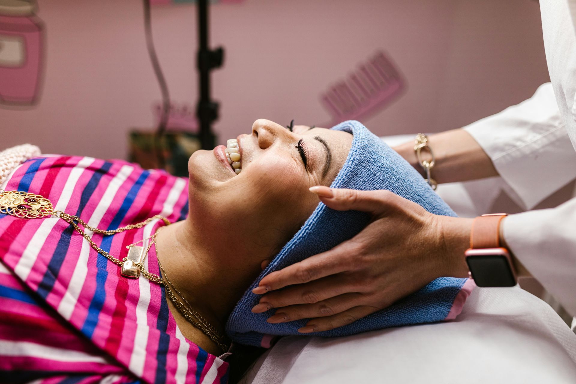 Woman receiving a facial treatment while lying on a spa bed, covered with a pink checkered towel.