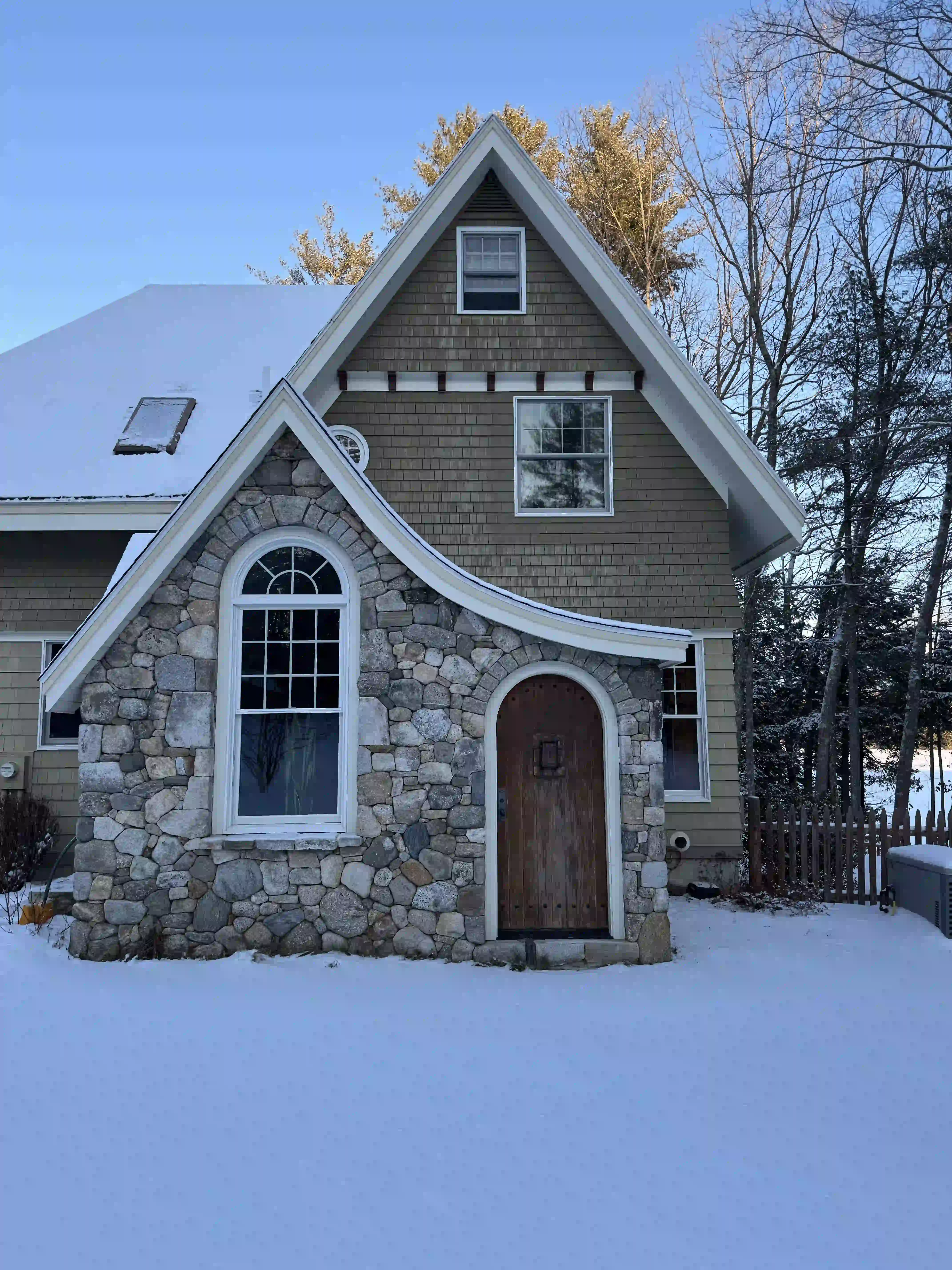 A house with a stone facade and a wooden door is covered in snow.