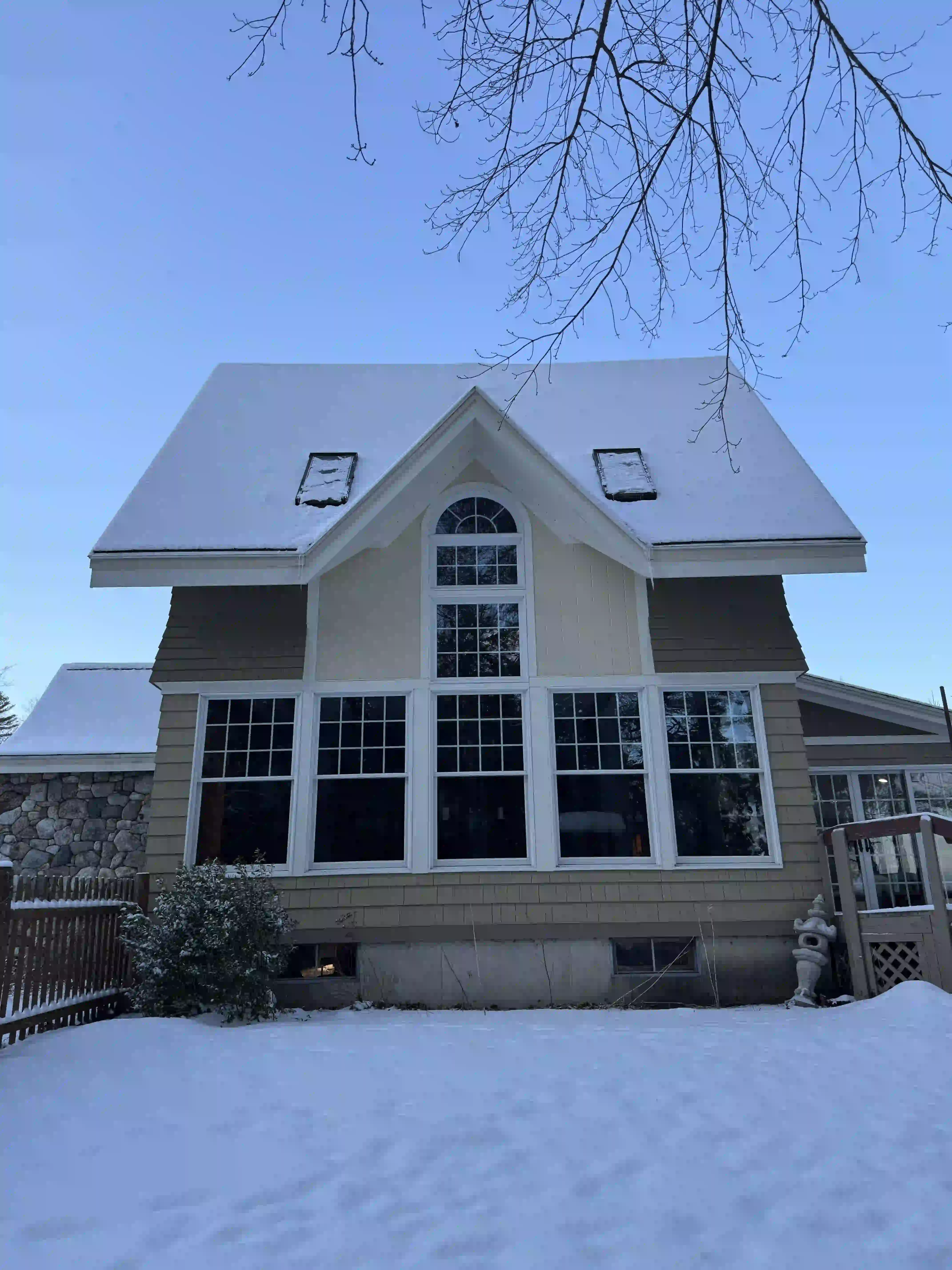 A house with a lot of windows is covered in snow.