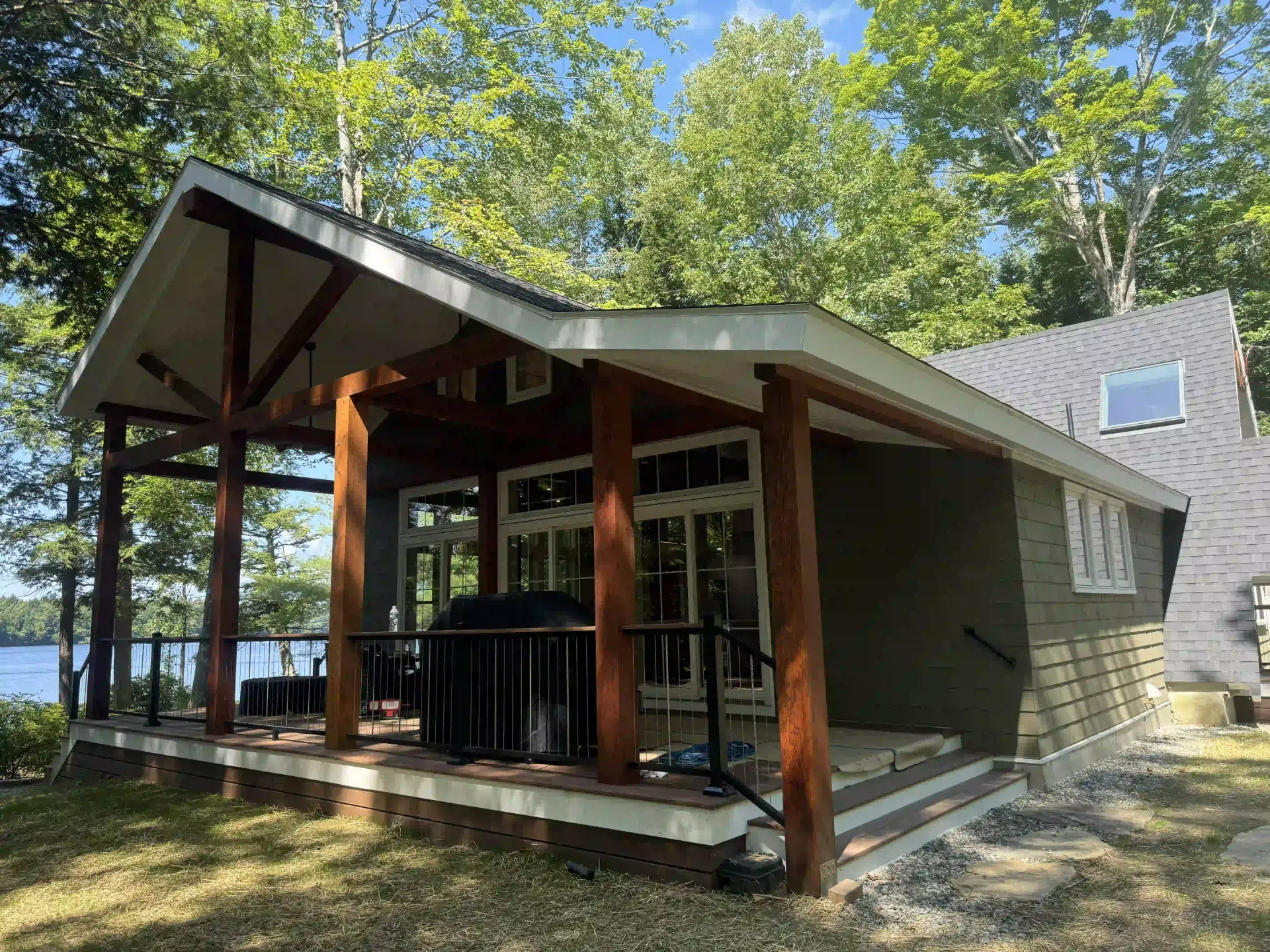 A small house with a porch overlooking a lake surrounded by trees.