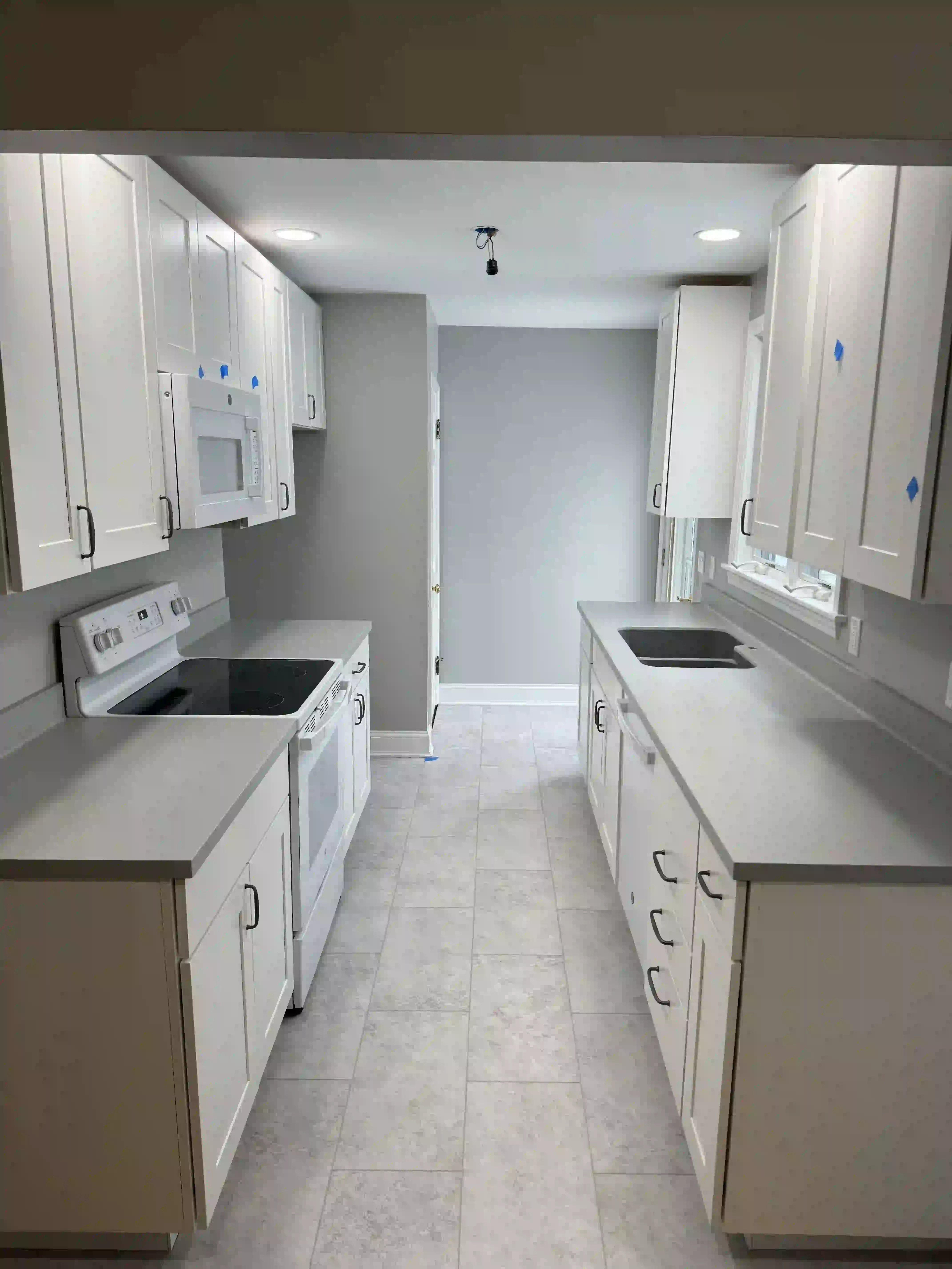 A kitchen with white cabinets , a stove , a microwave , and a sink.