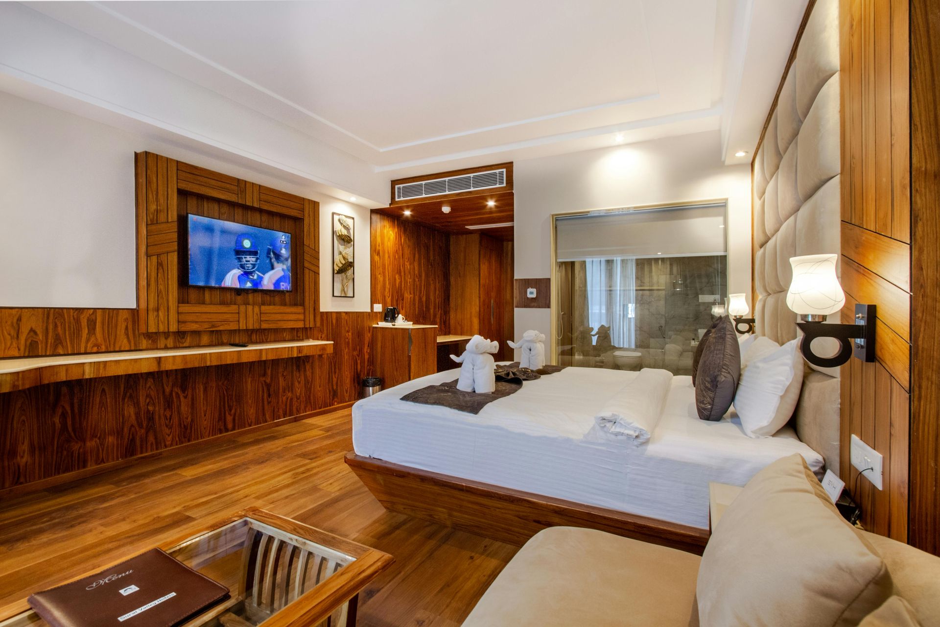 Hotel room with a bed, TV, wooden furniture, and a small seating area.
