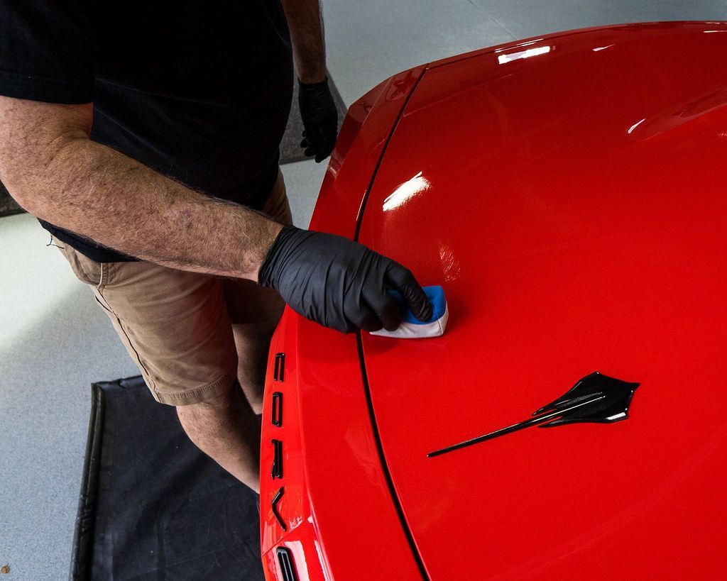 Gloved hand using a red tool to clean gray car door upholstery with a microfiber cloth