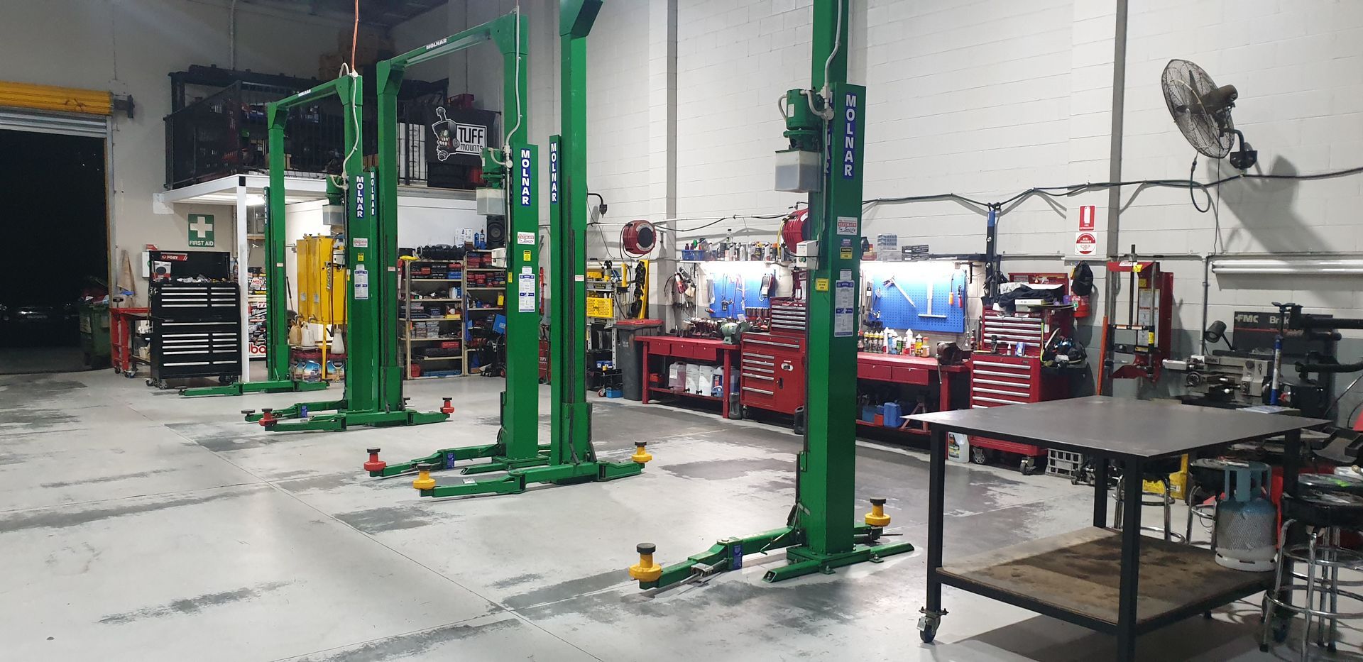 Inside a garage, three green vehicle lifts are lined up. Red toolboxes and a work table are visible — Cartech Australia in Albury, NSW