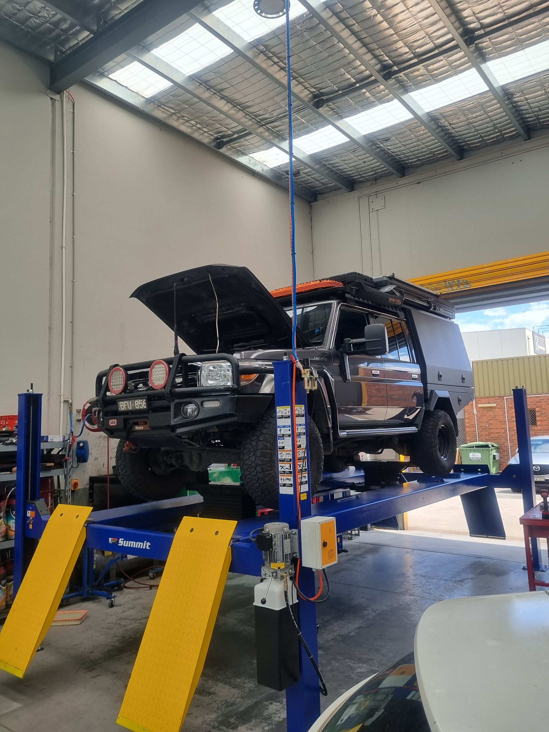 Dark 4WD on a blue and yellow car lift in a workshop, hood open — Cartech Australia in Albury, NSW