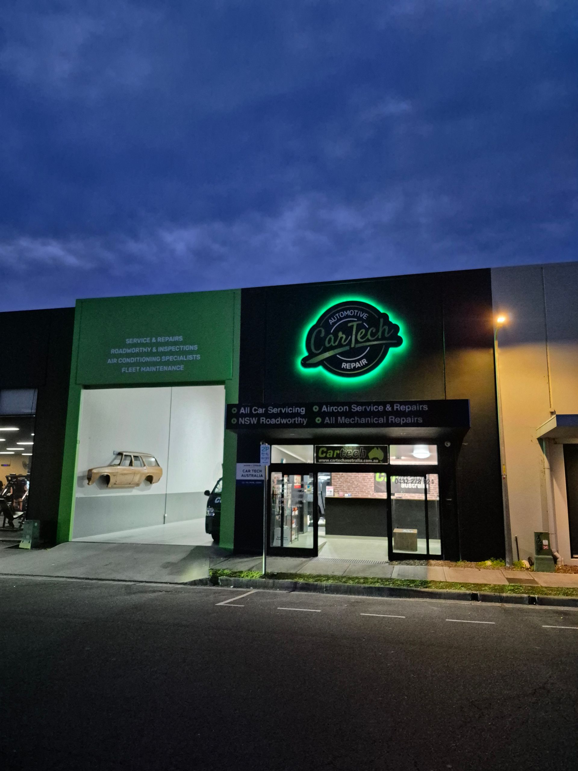 Green and black building with illuminated sign, large garage door, and entrance under a dark sky — Cartech Australia in Albury, NSW
