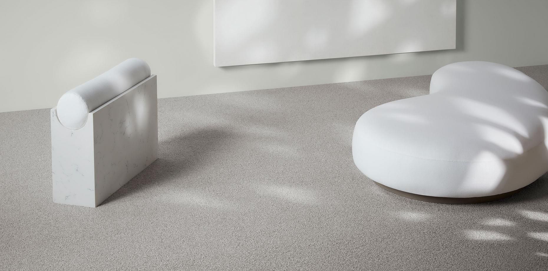 A white chair and ottoman are sitting on a carpeted floor in a room.