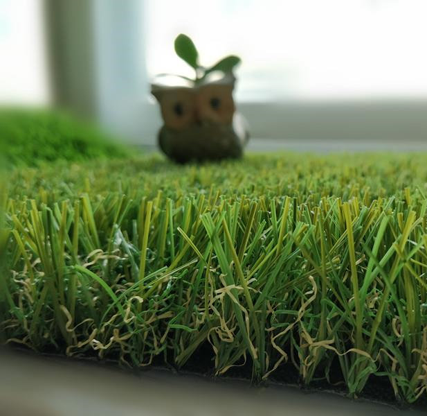 A close up of a piece of artificial grass with an owl in the background.