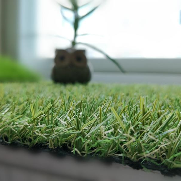 A close up of a piece of artificial grass with a plant in the background.