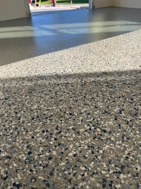 Close-up of a speckled, gray epoxy garage floor with the open doorway in the background.