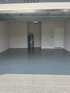 Empty garage with gray speckled floor, water heater, white door, and beige walls.