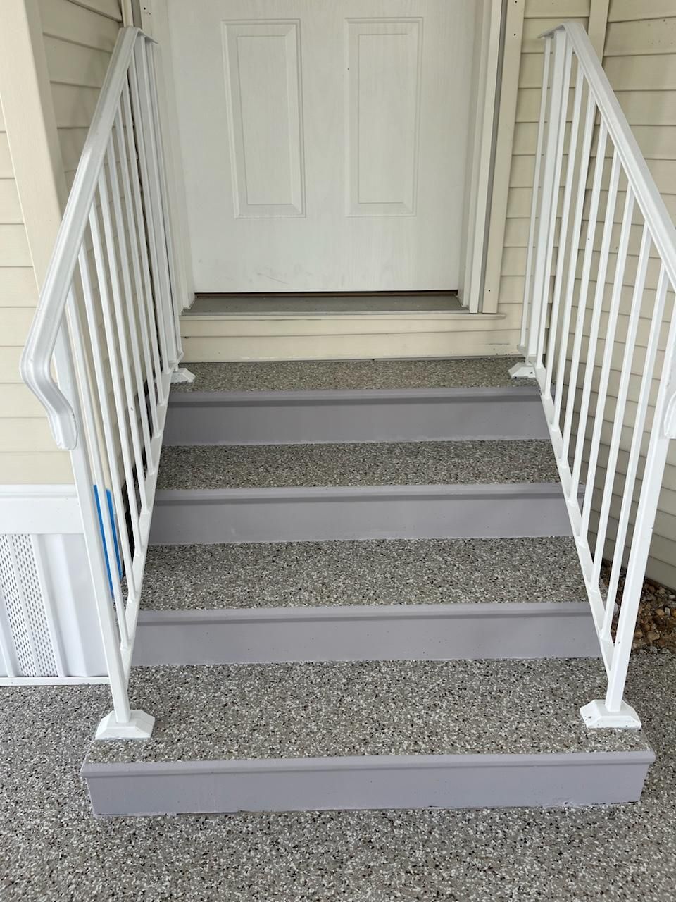 White-railed steps leading to a white door. The steps are gray, made of aggregate.