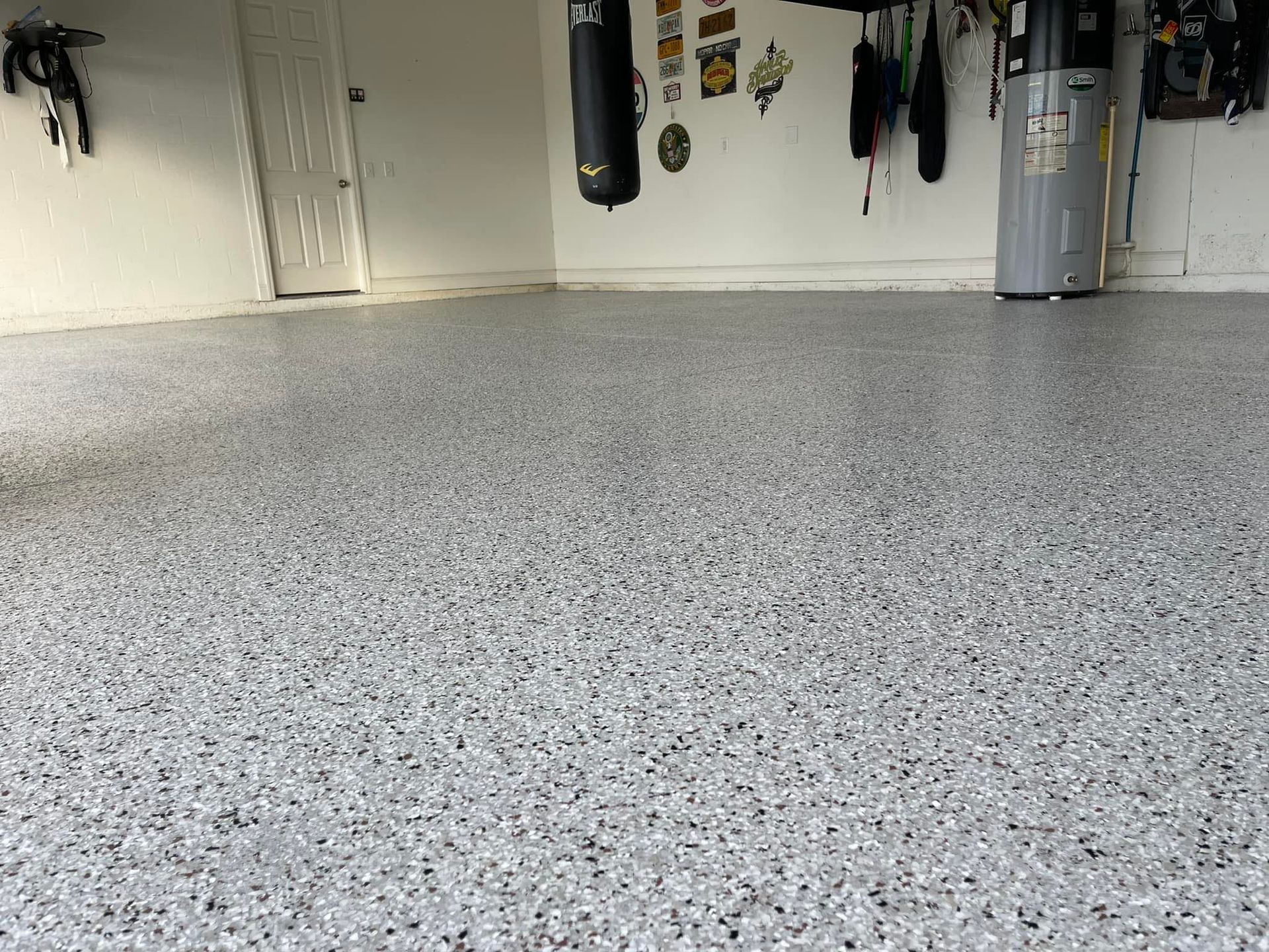 Epoxy-coated garage floor with gray and black flakes, white walls, and various items hanging.